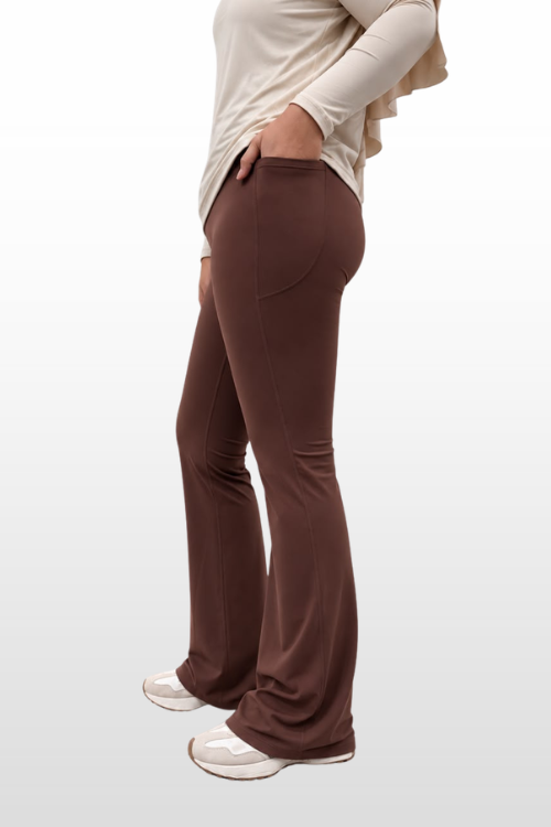 A model shown from the waist down wearing brown flared pants, a cream long-sleeve top, and white sneakers, set against a light gray gradient background.