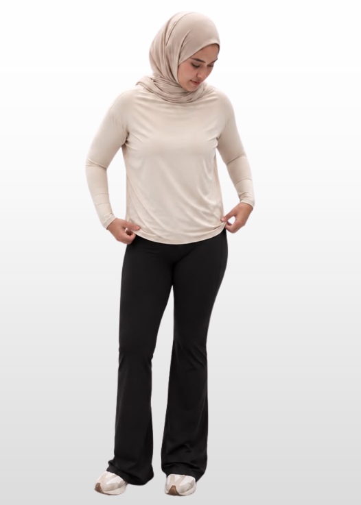 A woman wearing a light beige long-sleeve top, black pants, and a beige hijab stands against a light gray gradient background.