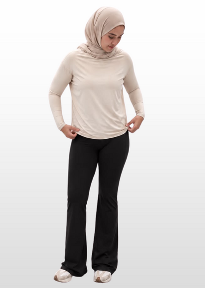 A woman wearing a light beige long-sleeve top, black pants, and a beige hijab stands against a light gray gradient background.