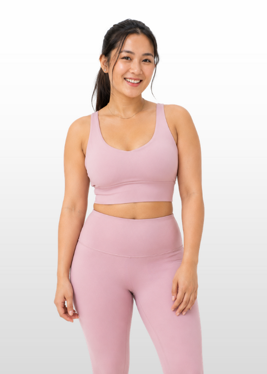A woman modeling a matching dusty pink activewear set consisting of a scoop-neck sports bra and high-waisted leggings, set against a clean white studio background.