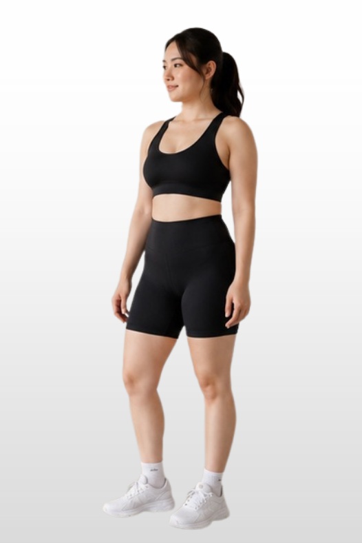A woman modeling a black sports bra and matching high-waisted athletic shorts against a light gray gradient background.