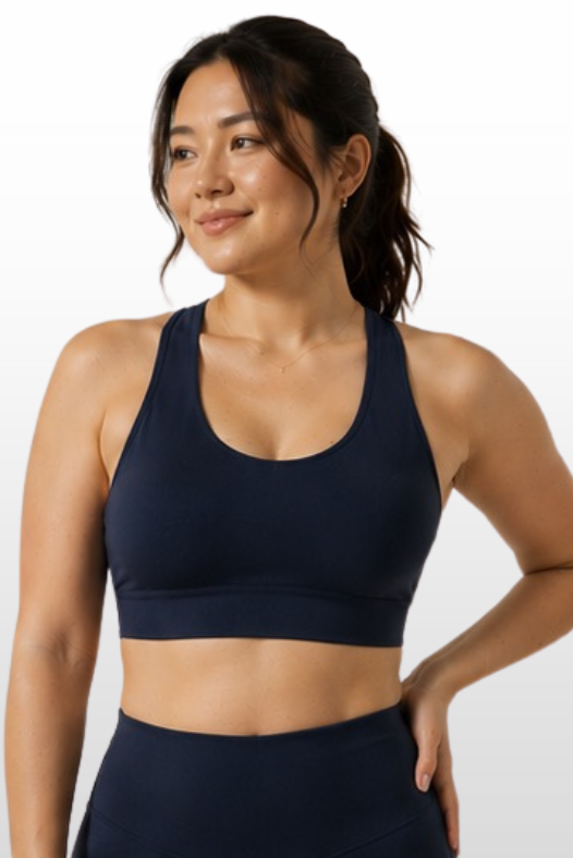 A woman wearing a dark navy blue sports bra and matching high-waisted leggings, shown from the waist up against a light gray gradient background.