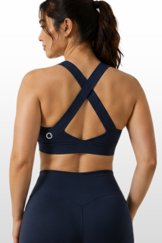 A woman shown from the back wearing a dark navy sports bra with crisscross straps and matching high-waisted leggings against a light gray studio background.