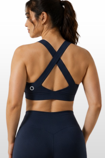A woman shown from the back wearing a dark navy sports bra with crisscross straps and matching high-waisted leggings against a light gray studio background.