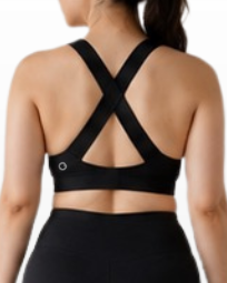 A woman viewed from the back wearing a black sports bra with crisscross straps and black fitted shorts, standing against a light gray studio background.