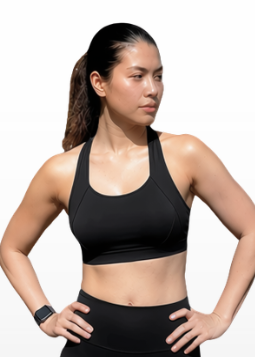 A woman modeling a black athletic sports bra and matching black biker shorts, paired with white crew socks and white sneakers, standing against a light gray gradient background.