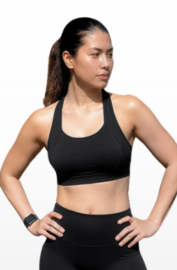 A woman modeling a black athletic sports bra and matching black biker shorts, paired with white crew socks and white sneakers, standing against a light gray gradient background.